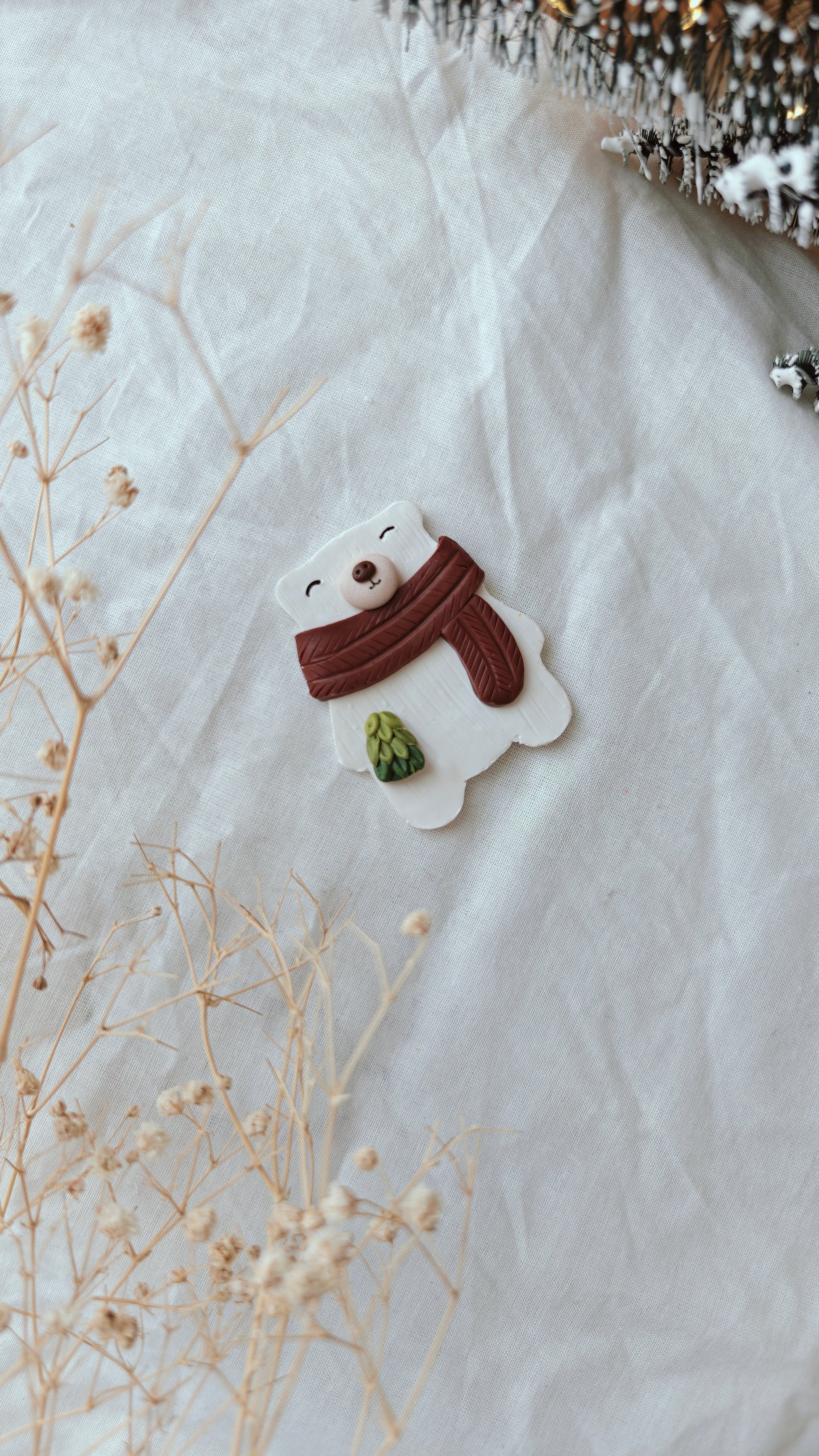 Snowman-shaped cookie with a brown scarf on a white marble surface with dried flowers.