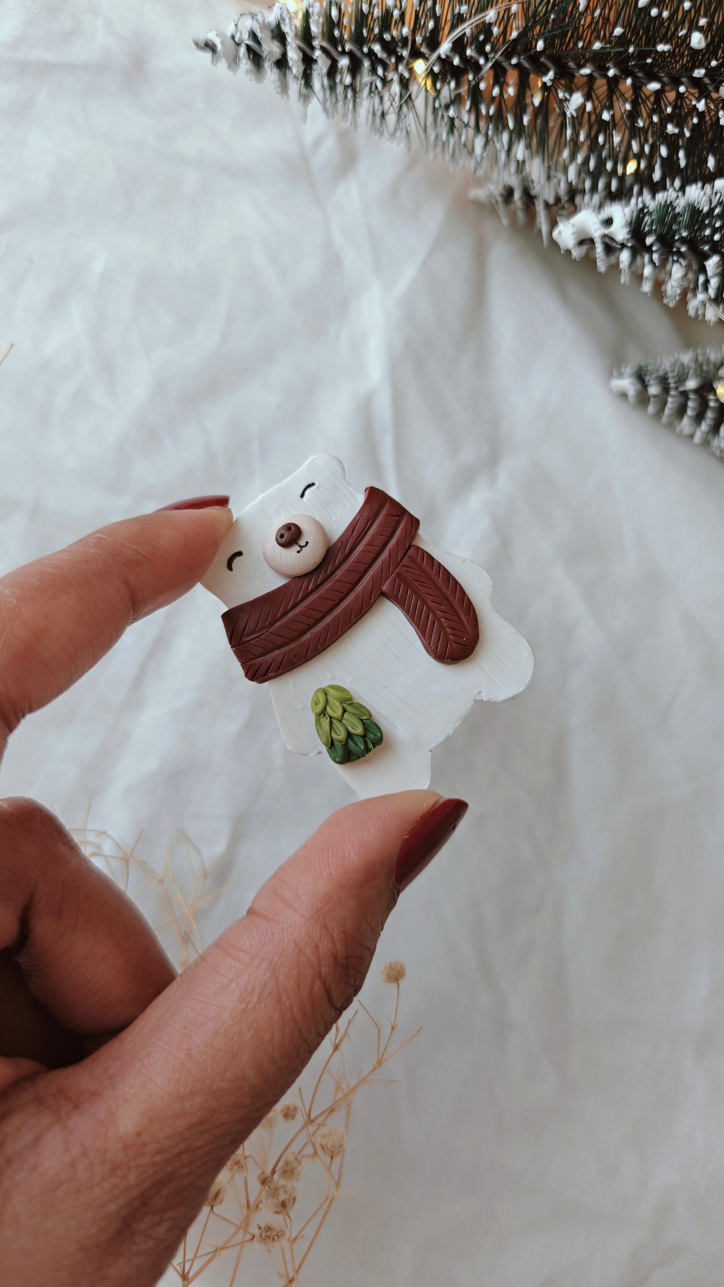 Hand holding a small snowman ornament with a brown scarf and green hat on a white background.